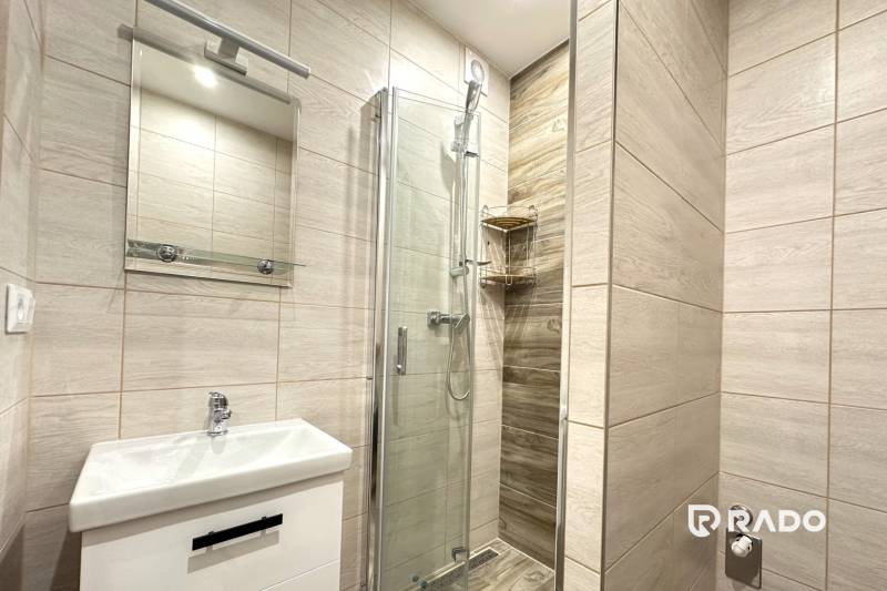 Badezimmer mit Waschbecken, Duschkabine und Spiegel in einer 2-Zimmer-Wohnung.