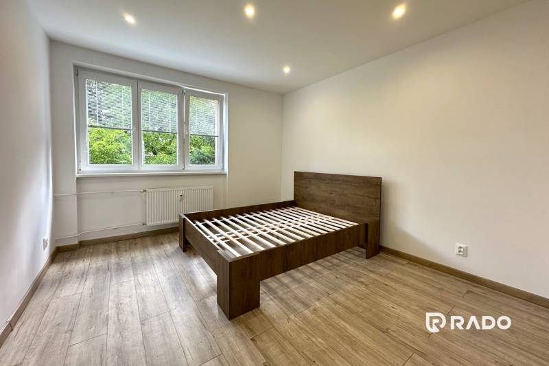 Helles Schlafzimmer mit Holzbett in einer 2-Zimmer-Wohnung mit großen Fenstern.