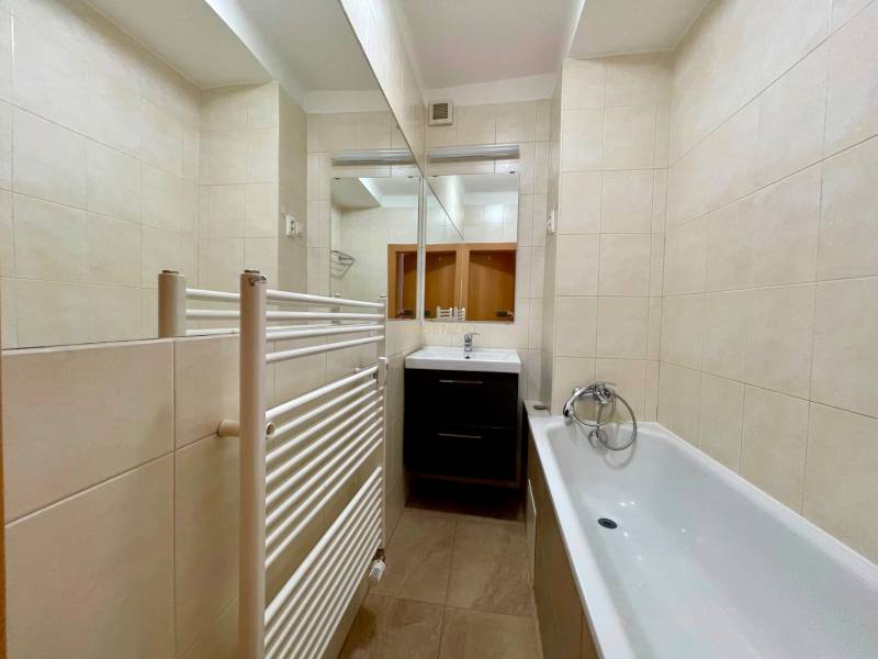 Badezimmer in einer 2-Zimmer-Wohnung mit Badewanne, Waschbecken, Spiegel und Heizkörper.