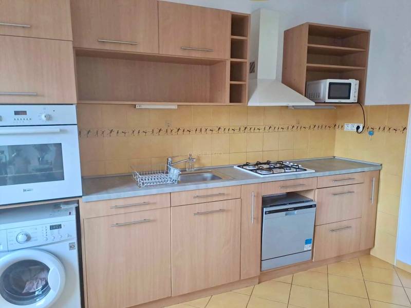 Küche mit Holzschränken, gelben Fliesen und eingebauten Geräten in einer 2-Zimmer-Wohnung.