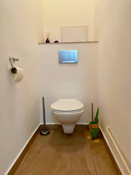 Toilette in einer 2-Zimmer-Wohnung mit Keramikfliesen und dekorativem Bürstenhalter.
