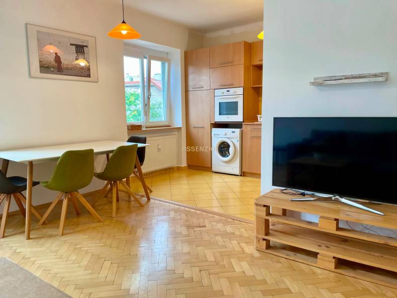 Wohnzimmer mit Küche, Holzboden, Fernseher und Esstisch in einer 2-Zimmer-Wohnung.