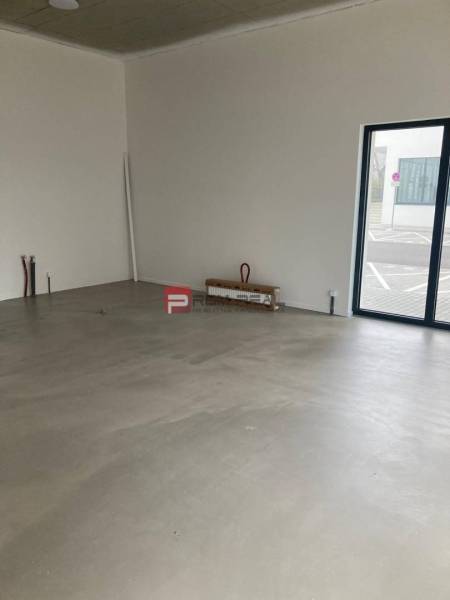 Ungeordnete Geschäftsräume mit großen Fenstern und Betonboden.