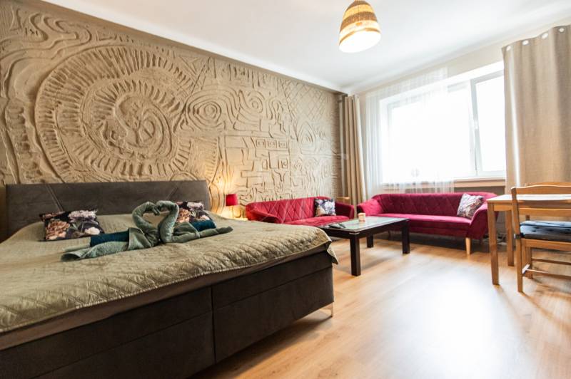 Ein Zimmer in einer 2-Zimmer-Wohnung mit einem Bett, roten Sofas und einem dekorativen Relief an der Wand.