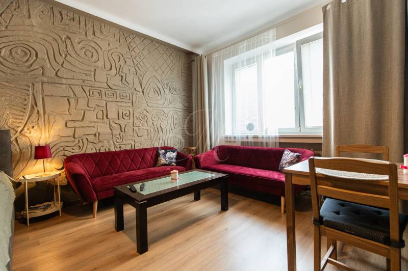 Wohnzimmer in einer Zweizimmerwohnung mit gemusterter Wand und roten Sofas.