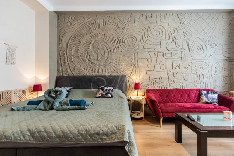 Stilvolles Schlafzimmer mit dekorativer Wand, Bett und rotem Sofa in einer 2-Zimmer-Wohnung.
