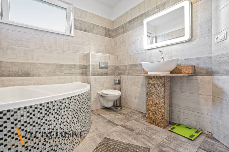 Ein Badezimmer in einem Einfamilienhaus mit stilvollen Keramikfliesen, einer Badewanne und einem Designer-Waschbecken.