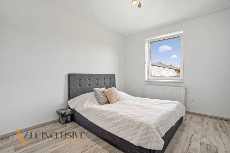 Schlafzimmer im Einfamilienhaus mit einfachem Bett und Fenster, helle Holzböden.