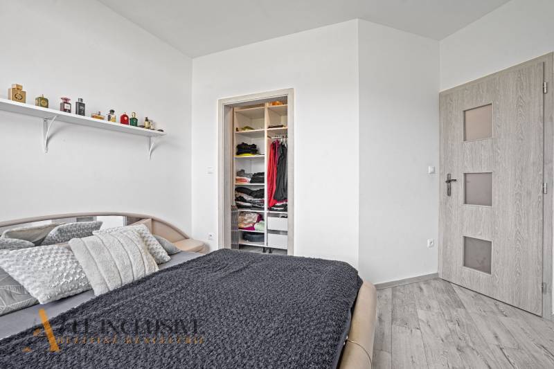 Schlafzimmer mit Bett im Einfamilienhaus, offener Kleiderschrank und Regal mit Parfums.