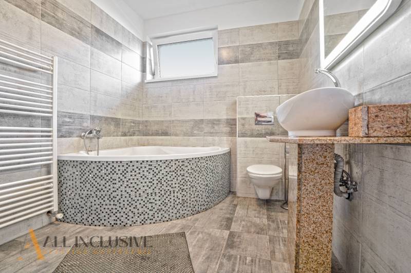 Ein Badezimmer in einem Einfamilienhaus mit Badewanne, Waschbecken und Toilette, gefliest mit hellen Fliesen.