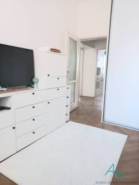 Weißes Wohnzimmer in einer 4-Zimmer-Wohnung mit Fernseher, Schränken und Holzboden.