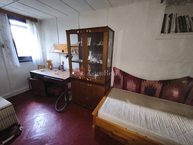 Ein Zimmer mit einem Holzboden, einem Schrank, einem Tisch und einem Bett in einer Hütte.