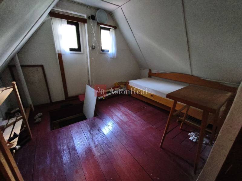 Ein Zimmer im Obergeschoss einer Hütte mit einem Boden in Holzoptik, einfacher Einrichtung und Fenstern.
