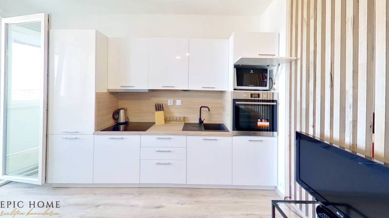 Küche in einer Einzimmerwohnung mit weißer Küchenzeile, Herd, Backofen und offener Balkontür.