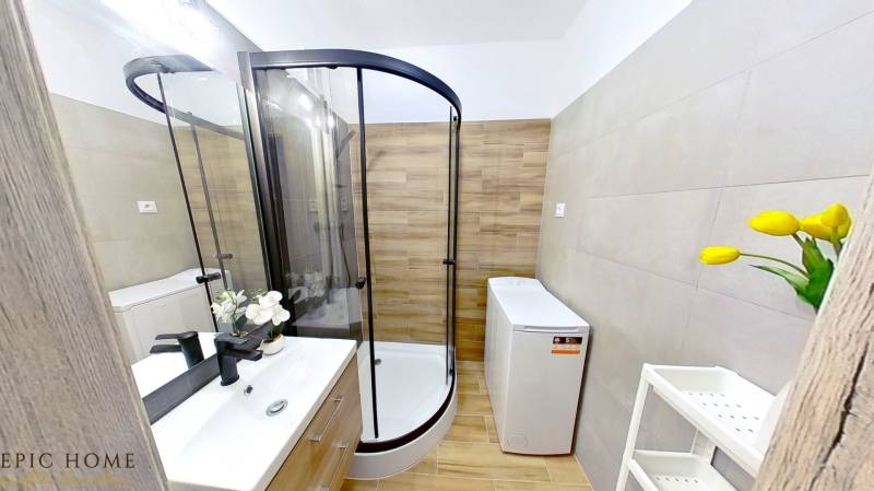 Badezimmer mit Eckdusche, Waschmaschine und Waschbecken in einer Einzimmerwohnung.