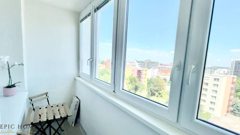Ein verglaster Balkon mit Blick auf Bratislava, eine Pflanze im Blumentopf, ein Stuhl und ein Tisch.