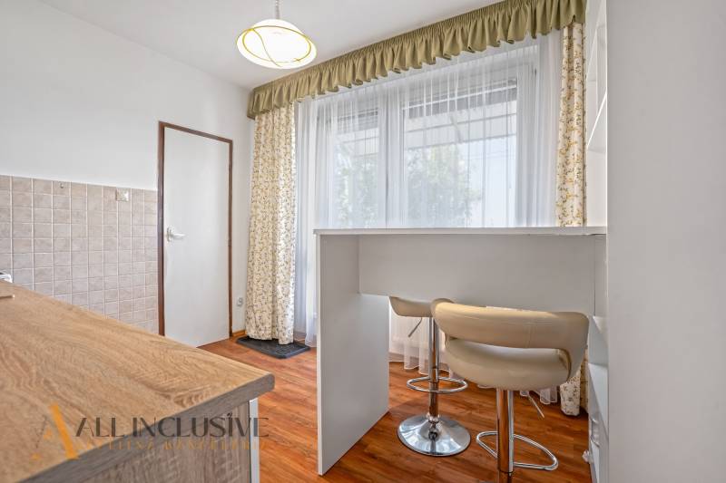 Küche in einer 2-Zimmer-Wohnung mit Bartresen, Vorhängen und hellen Möbeln.