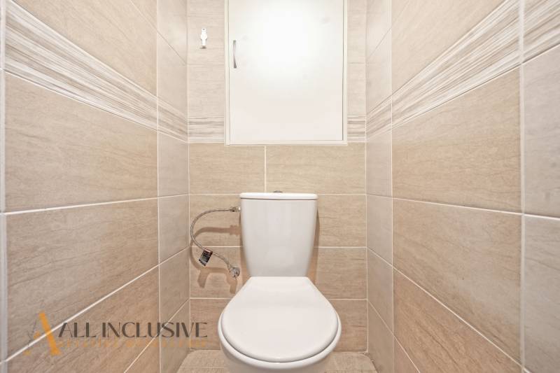 Toilette mit beigefarbenen Fliesen in einer 2-Zimmer-Wohnung.