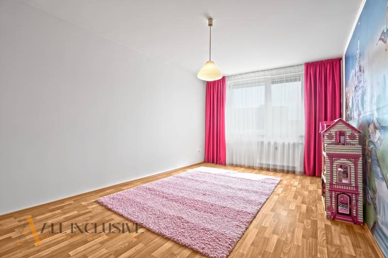 Kinderzimmer in einer Zweizimmerwohnung mit rosa Teppich und Vorhängen.