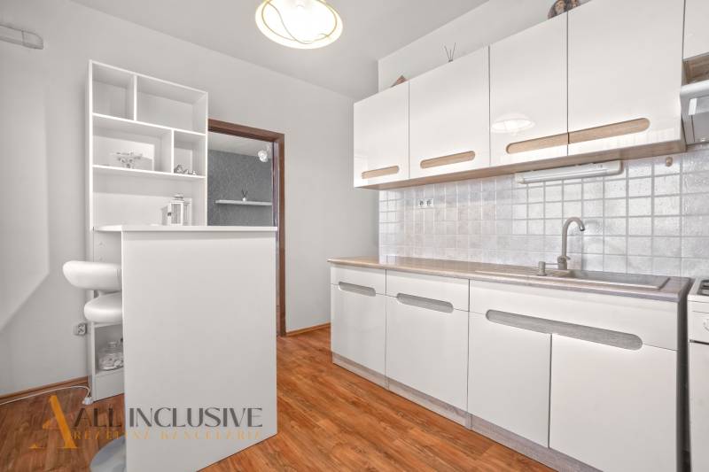 Weiße Küche mit Holzboden und Bartresen in einer 2-Zimmer-Wohnung.