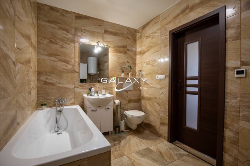 Ein Badezimmer in einem Einfamilienhaus mit Badewanne, Waschbecken und Toilette in warmen Fliesentönen.