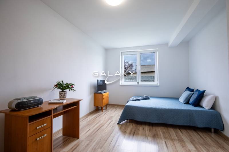 Ein Zimmer in einem Einfamilienhaus mit einem Bett, einem Schreibtisch und einem Fernseher auf einem hellen Boden.