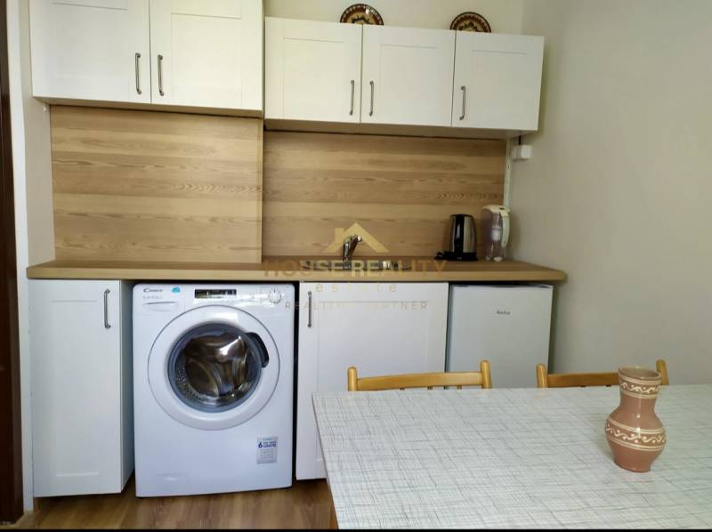 Küche in einer Einzimmerwohnung mit weißen Schränken, Waschmaschine, Spüle und Esstisch.