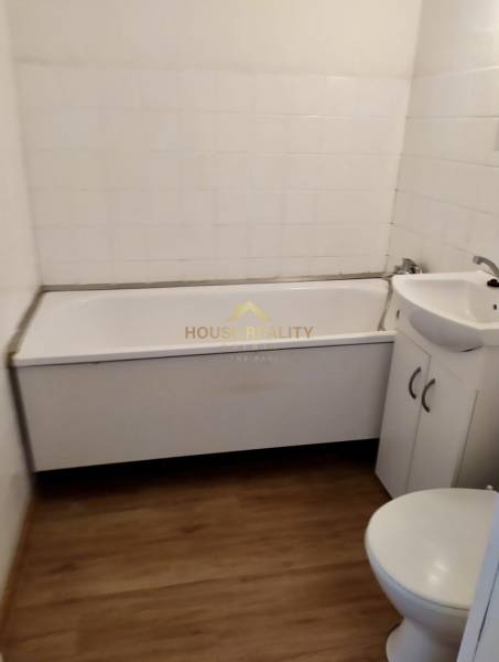 Badezimmer in einer Einzimmerwohnung mit Badewanne, Waschbecken und Toilette, Fliesen in Holzoptik.