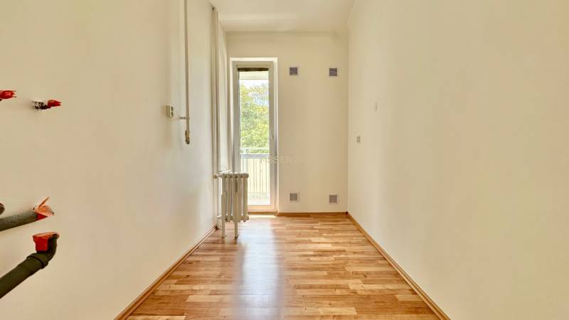 Ein Zimmer mit Holzboden und Balkon in einer 3-Zimmer-Wohnung, weiße Wand, Heizkörper.