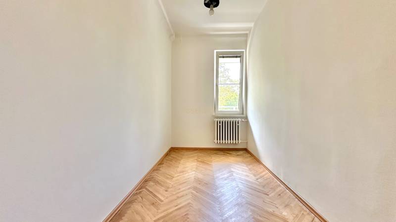Ein Zimmer mit hellen Wänden, Holzboden, Heizkörper und Fenster in einer 3-Zimmer-Wohnung.