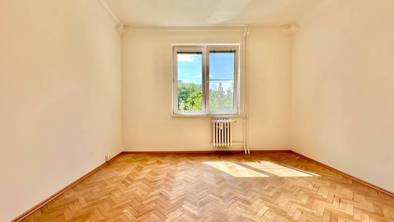 Ein leerer Raum in einer 3-Zimmer-Wohnung mit Parkettboden und einem Fenster mit Blick ins Grüne.