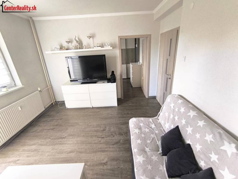 Wohnzimmer in einer Zweizimmerwohnung mit einem Sofa und einem Fernseher auf einer Kommode.