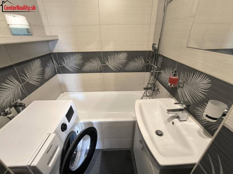Badezimmer in einer 2-Zimmer-Wohnung mit Waschmaschine, Badewanne, Waschbecken und dekorativen Fliesen.