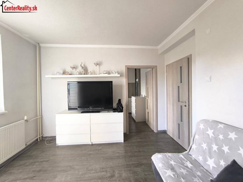 Wohnzimmer in einer 2-Zimmer-Wohnung mit einem Fernseher auf einer weißen Kommode und einem Sofa.