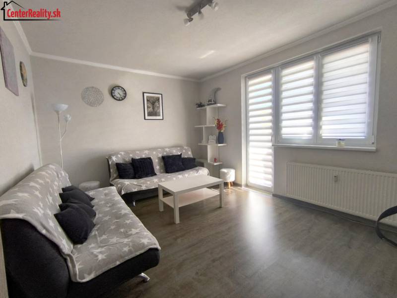 Wohnzimmer in einer Zweizimmerwohnung mit Sofas und einem Tisch, Licht scheint durch die Jalousien.