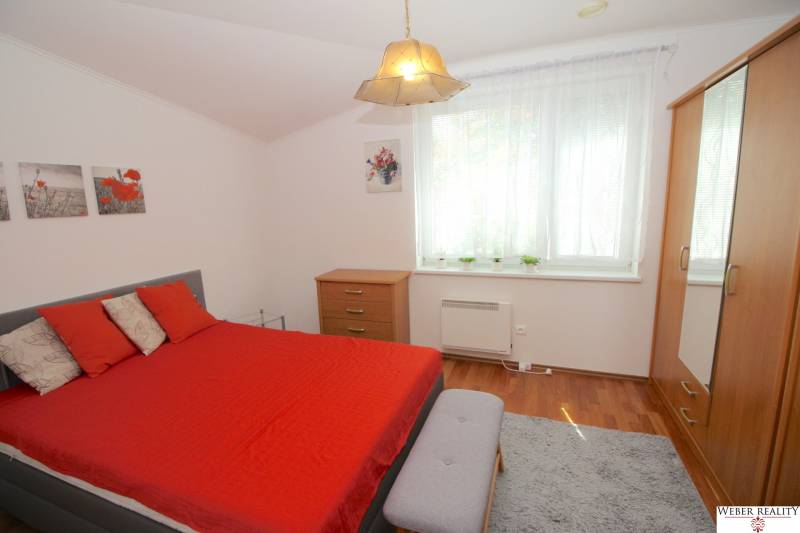 Ein Schlafzimmer in einem Einfamilienhaus mit roter Bettwäsche, einer Kommode und einem großen Fenster.