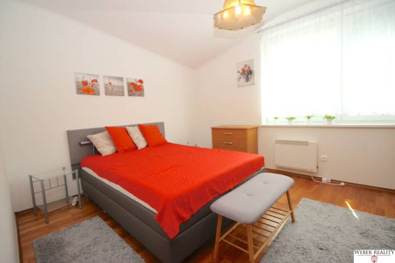 Schlafzimmer im Einfamilienhaus mit grauem Bett, roten Decken und Holzmöbeln.