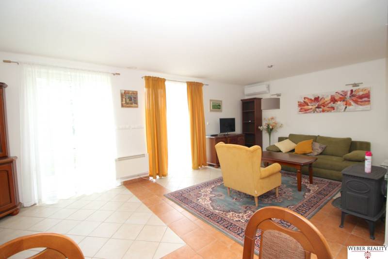 Wohnzimmer in einem Einfamilienhaus mit Sofa und Sessel, dekoriert mit Bildern und Vorhängen.