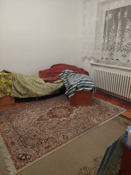 Ein Zimmer in einem Einfamilienhaus mit einem Bett, einem Teppich und Spitzenvorhängen.