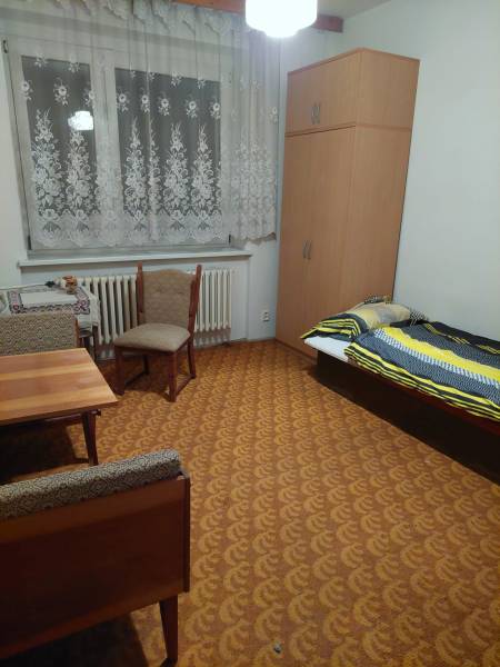 Ein Zimmer eines Einfamilienhauses mit Bett, Schrank, Tisch und Stühlen, in warmen Farben gehalten.