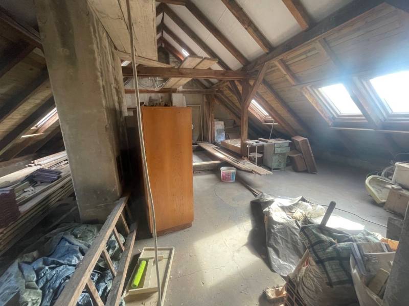 Dachboden in einem Einfamilienhaus mit Balken, Dachfenstern und gelagerten Gegenständen.