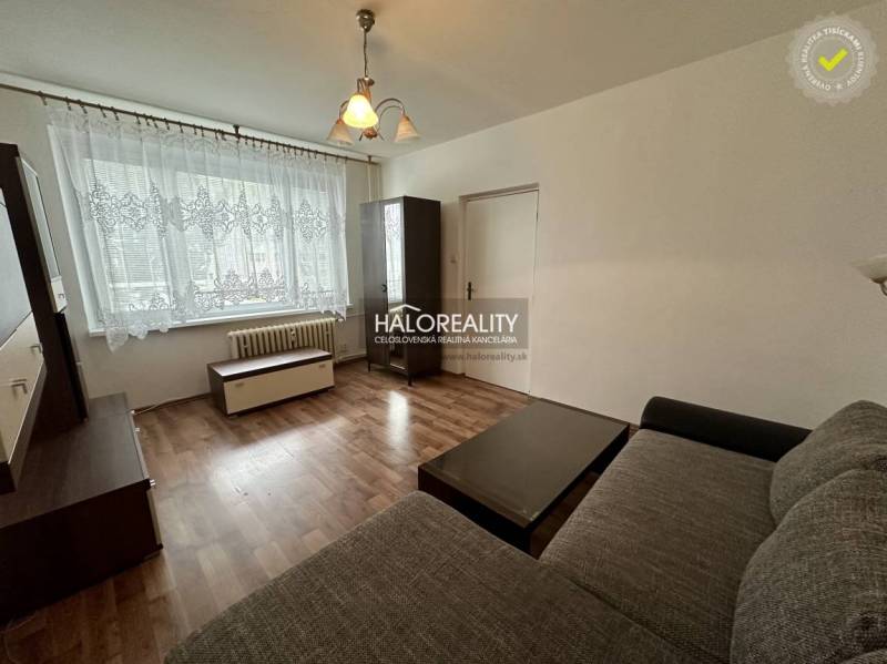 Wohnzimmer in einer Einzimmerwohnung mit Fenster, Vorhängen, dunklen Möbeln und Sofa.