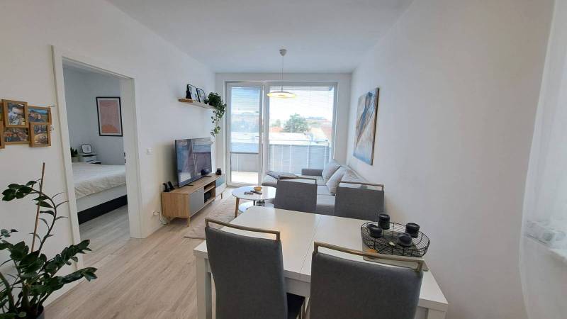 Helles Wohnzimmer mit weißen Möbeln und Zugang zum Schlafzimmer in einer Zweizimmerwohnung.