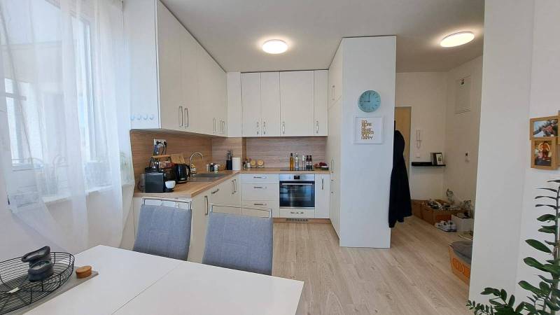 Küche in einer 2-Zimmer-Wohnung mit weißer Küchenzeile, Esstisch und Holzboden.