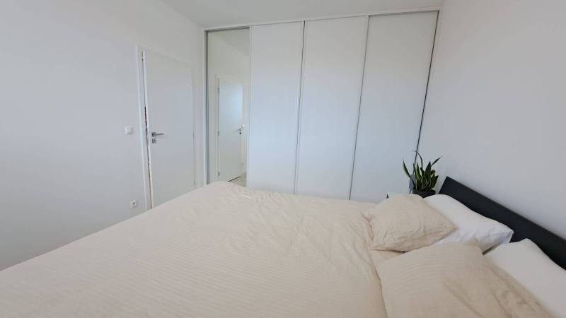Schlafzimmer mit Bett und Einbauschrank in einer 2-Zimmer-Wohnung, mit einer Pflanze auf dem Nachttisch.
