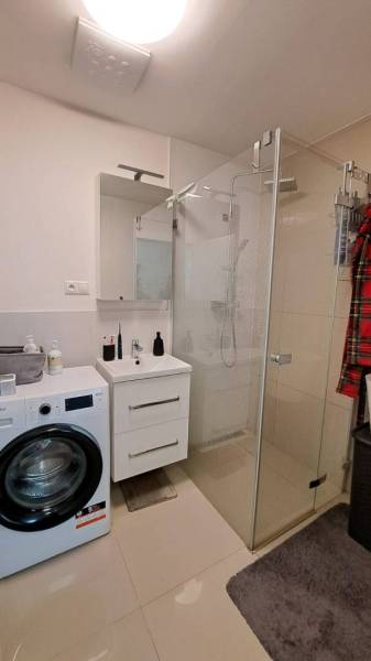 Badezimmer mit Waschmaschine, Duschkabine und Waschbecken in einer 2-Zimmer-Wohnung.