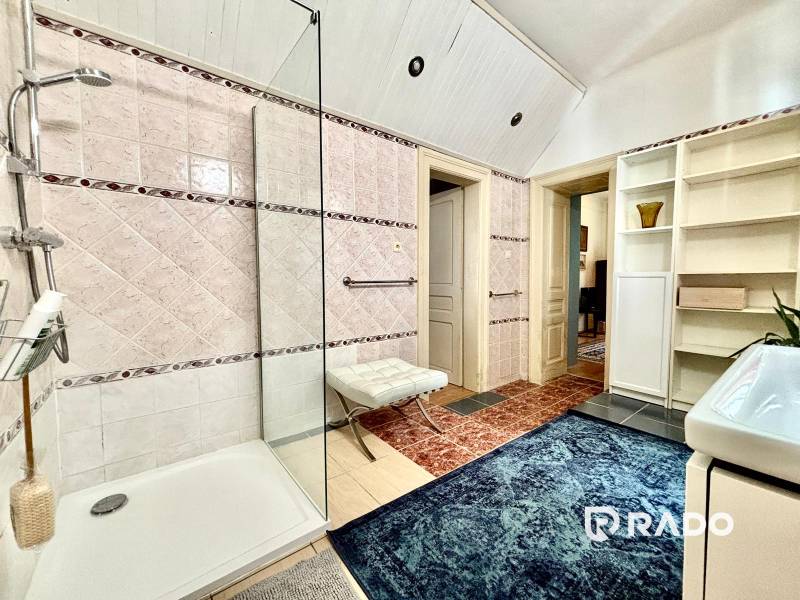 Badezimmer in einer 2-Zimmer-Wohnung mit Duschkabine, Teppich und Regalen zur Aufbewahrung.