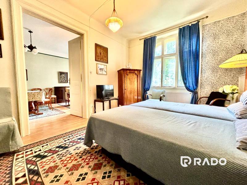 Schlafzimmer in einer 2-Zimmer-Wohnung mit Bett, blauen Vorhängen und orientalischem Teppich.