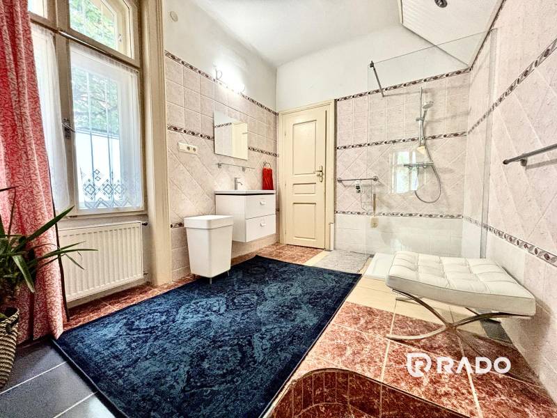 Badezimmer in einer 2-Zimmer-Wohnung mit Fenster, Badewanne und blauem Teppich.