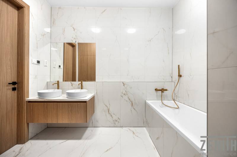 Badezimmer mit Spiegel, Doppelwaschbecken und Badewanne in einer 3-Zimmer-Wohnung.